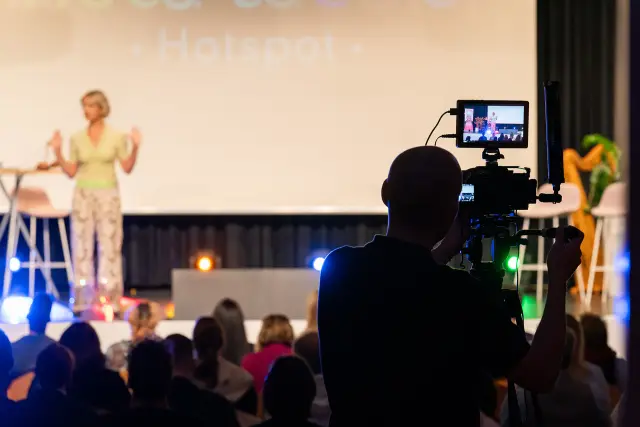 Kamera im Saal filmt eine Rednerin auf der Bühne