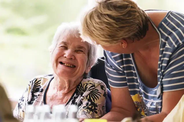Pflegerin und Seniorin lachen zusammen
