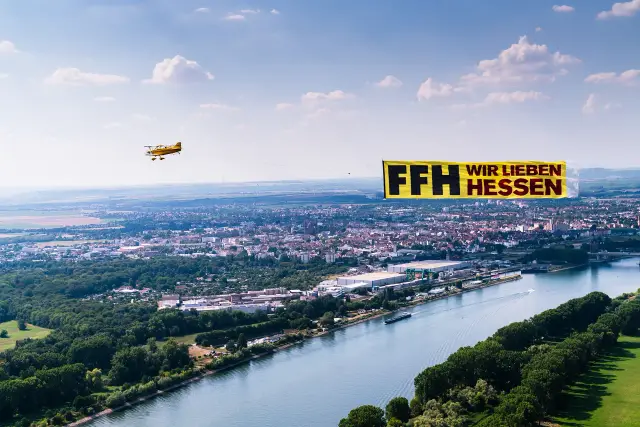 Flugzeug mit Werbebanner über einer Stadt am Fluss